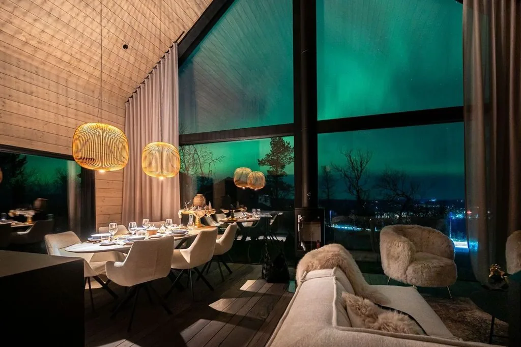Dining and living area of Grand Hideaway with the aurora glowing through the glass wall