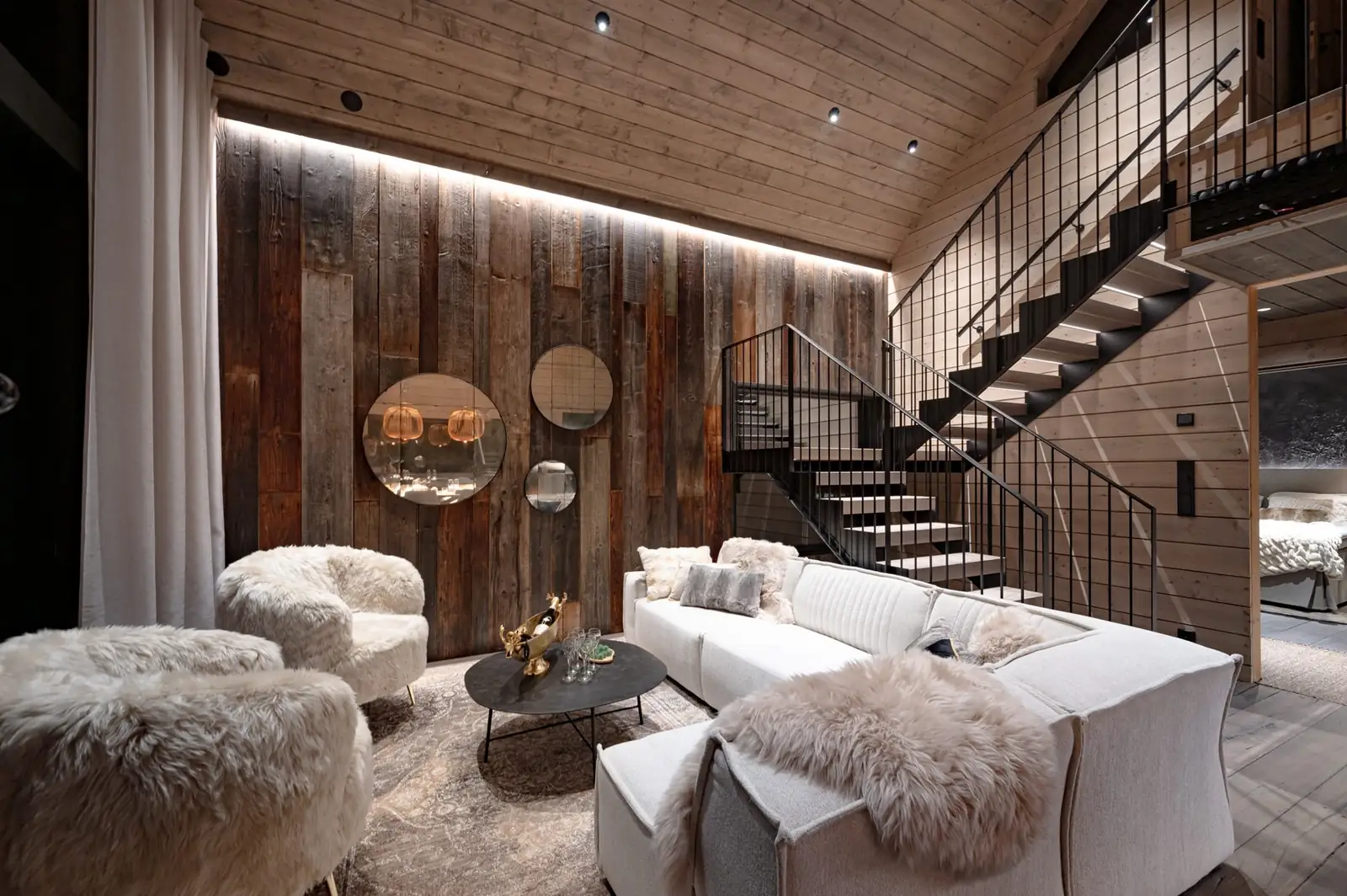 Lounge with sheepskin chairs, reclaimed wood wall and staircase in Grand Hideaway