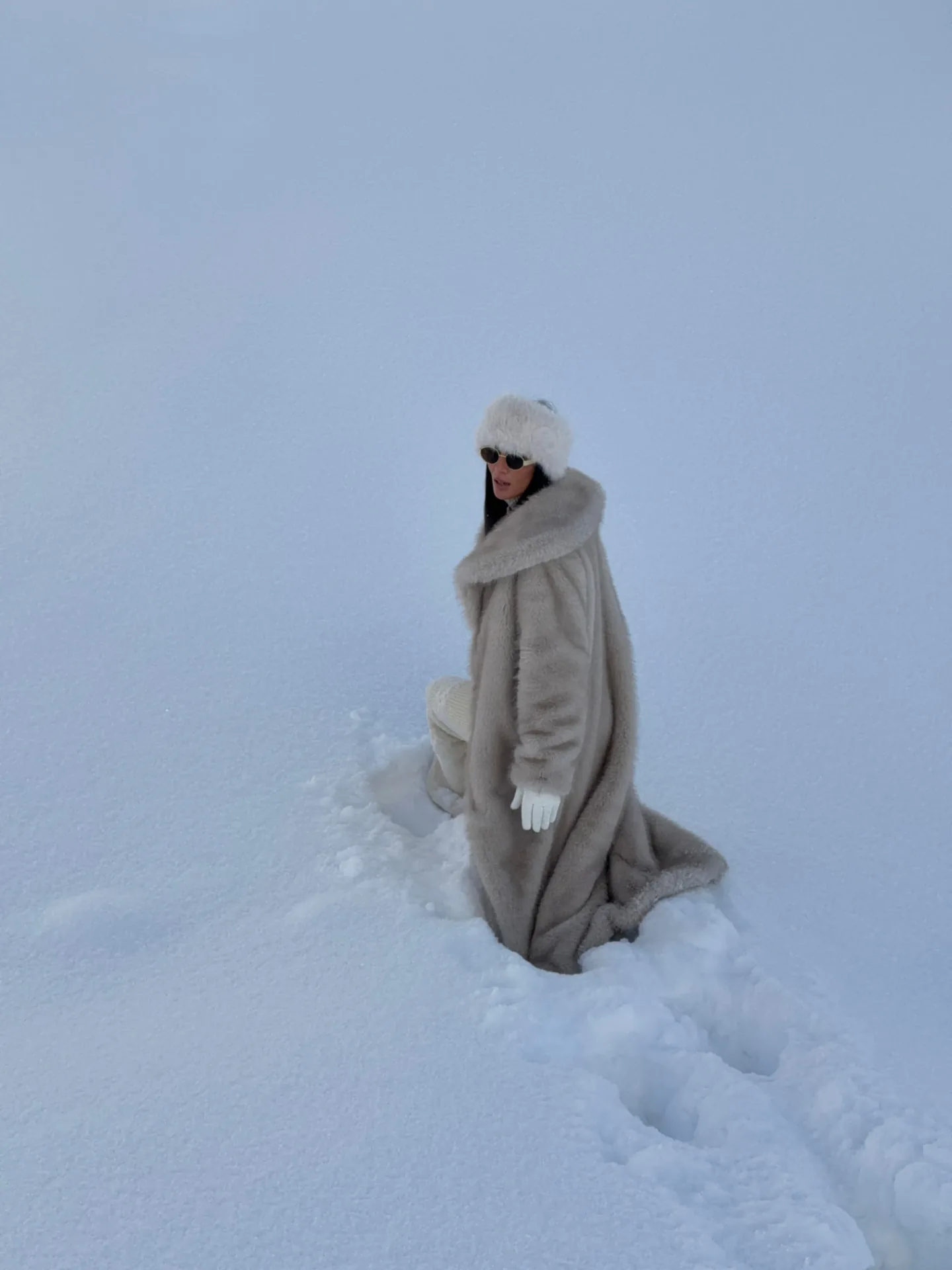 Guest in a long fur coat standing in an open snowy field at Aura